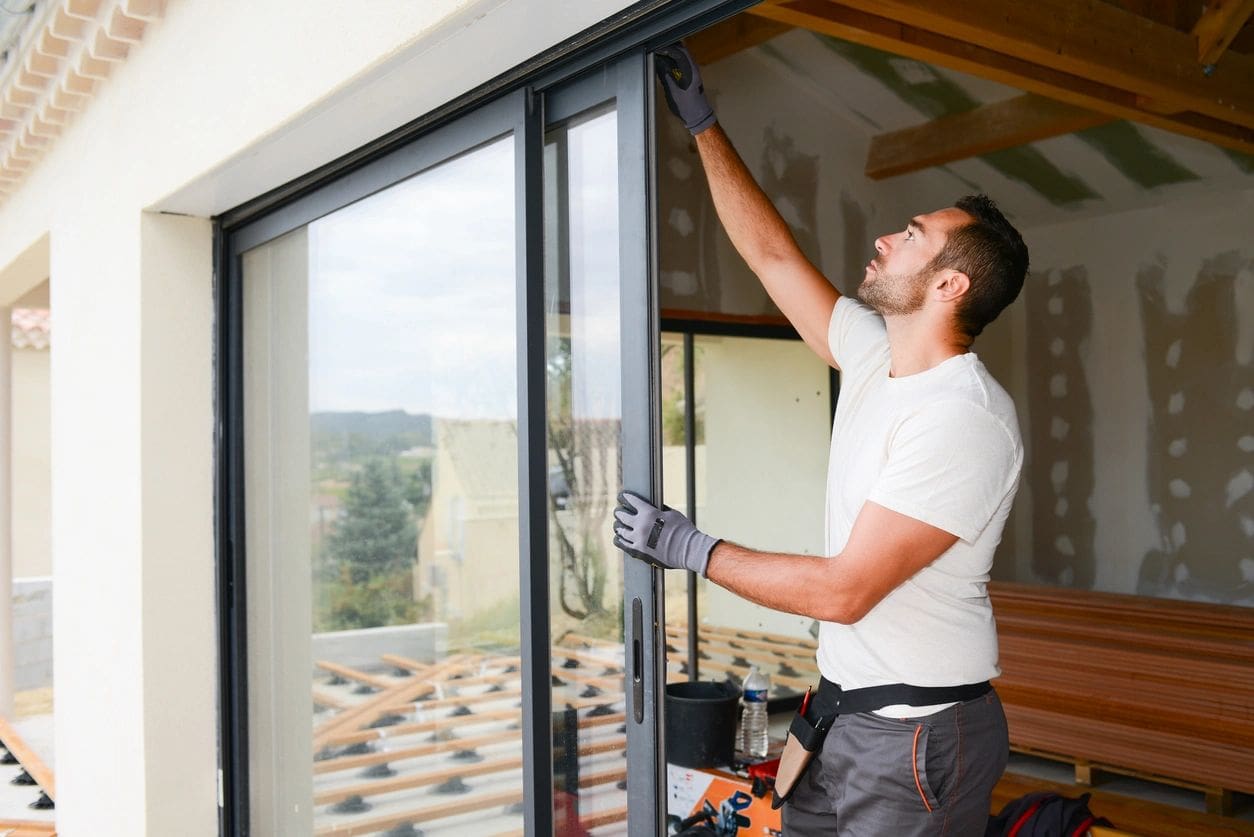 A man in white shirt and black pants standing next to window.